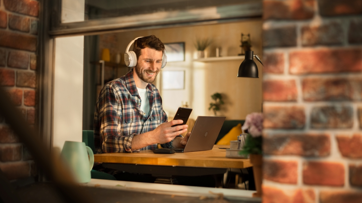 nowy ebok, mężczyzna ze słuchawkami na uszach, przed laptopem ze smartfonem w ręku