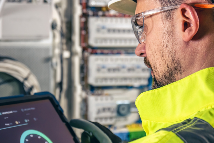 Pracownik w odzieży ochronnej obsługujący tablet przy rozdzielnicy